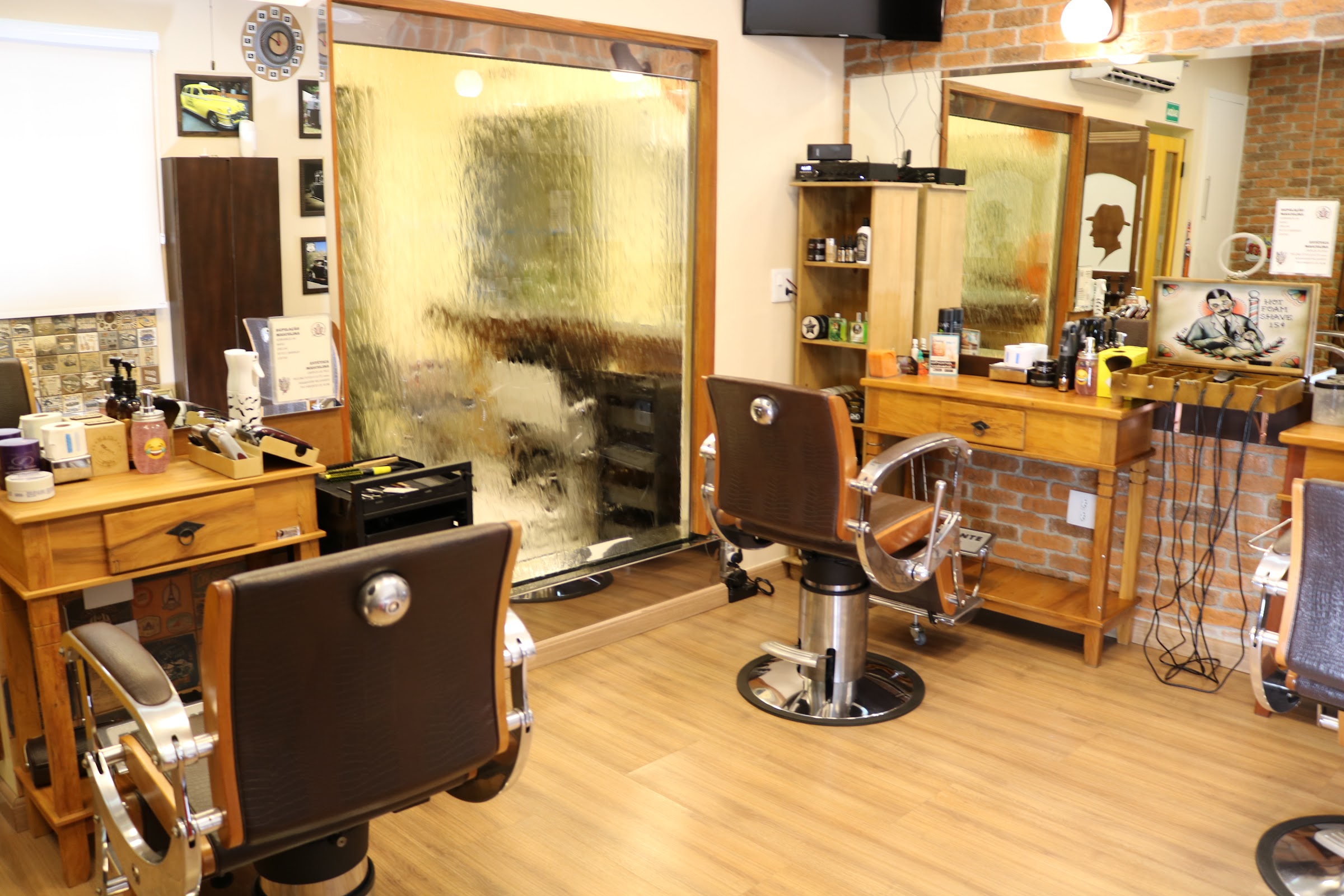 Interior da Oficina do Cabelo (Pinheiros): balcões de madeira, parede de tijolo e cadeiras de couro
